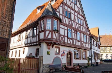 Un edificio tradicional de entramado de madera con estructura de madera marrón rojizo, tejado de tejas y una torreta en la esquina en un día soleado.