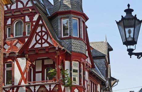 Vista de cerca de un edificio de entramado de madera rojo y blanco con tejado de pizarra gris, y una farola negra ornamentada en primer plano.