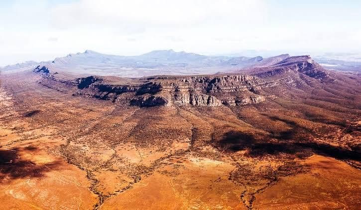 Eine Luftaufnahme einer weiten, trockenen Landschaft mit einer kreisförmigen Felsformation in der Mitte und Bergen am Horizont.