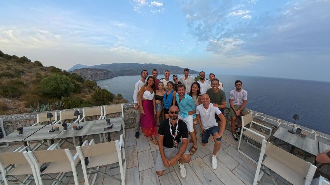 Un grupo de WeRoad posa para una foto en una terraza panorámica con vistas a una bahía de acantilados bajo un cielo nublado.