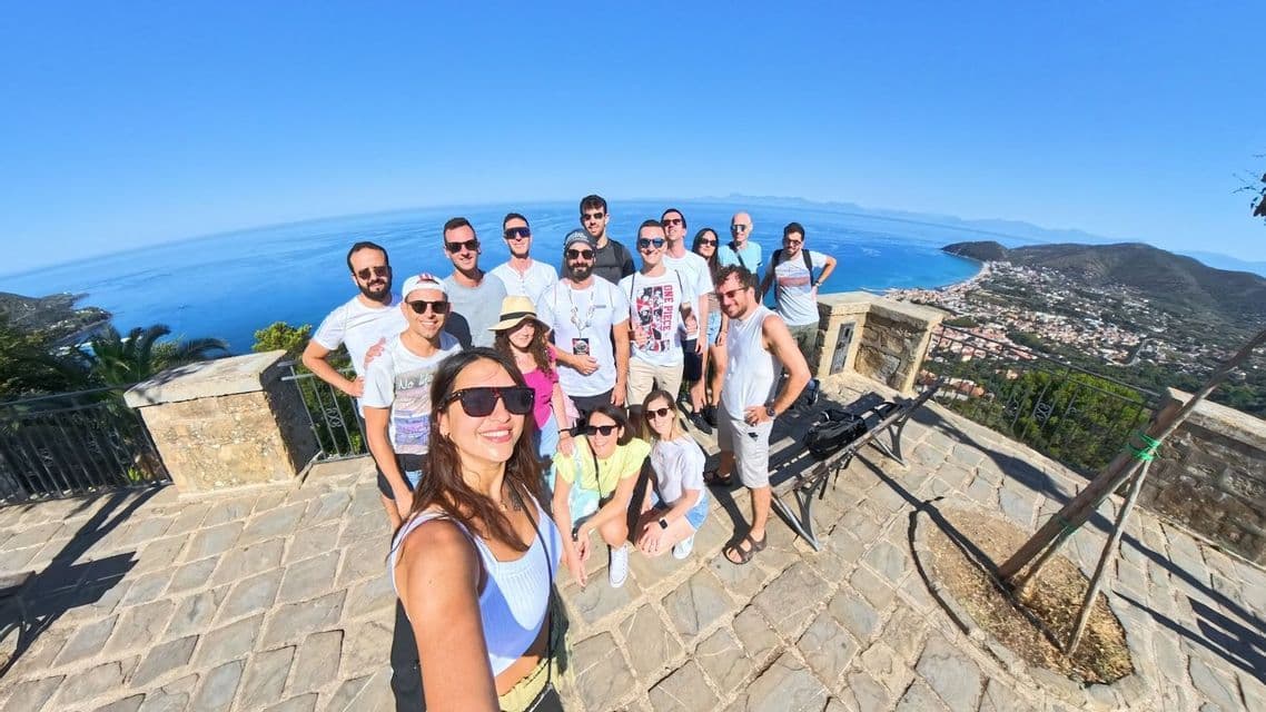 Un grupo de WeRoad se hace un selfie en un mirador de piedra con vistas a un pueblo costero y el mar azul