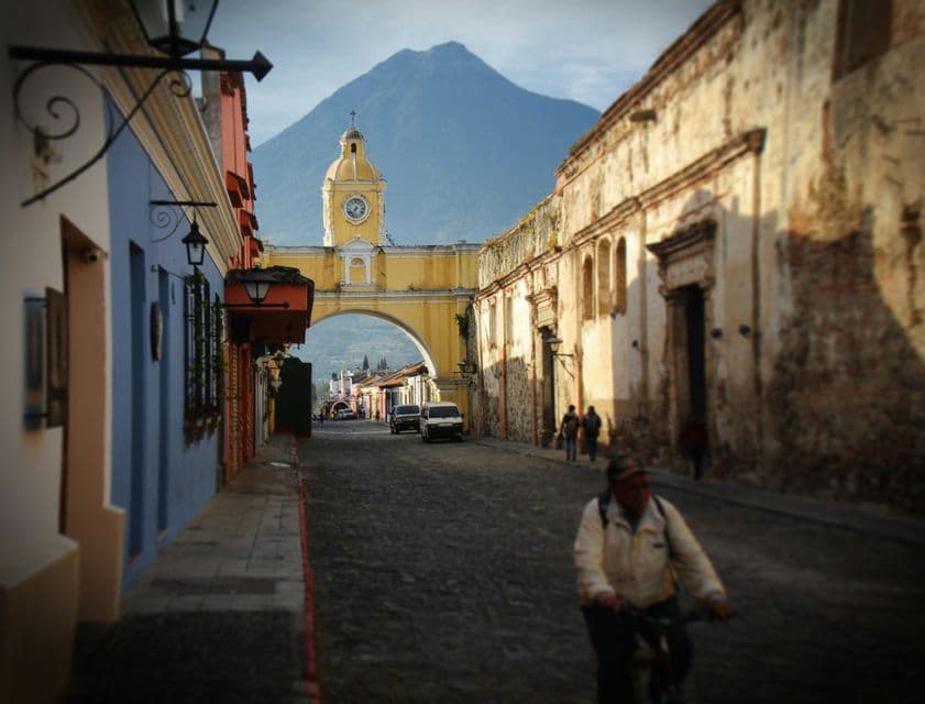 Vue d'une rue pavée avec des bâtiments coloniaux menant à une arche jaune, un volcan en arrière-plan.