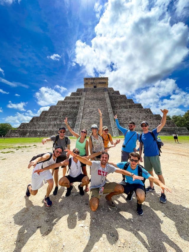 Eine Gruppe von WeRoad-Freunden posiert für ein Foto vor einer großen steinernen Stufenpyramide unter strahlend blauem Himmel.