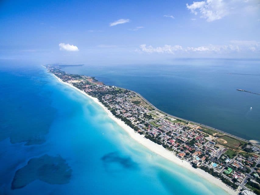 An aerial view of a long peninsula featuring a white sand beach, a coastal town, and contrasting turquoise and deep blue waters.
