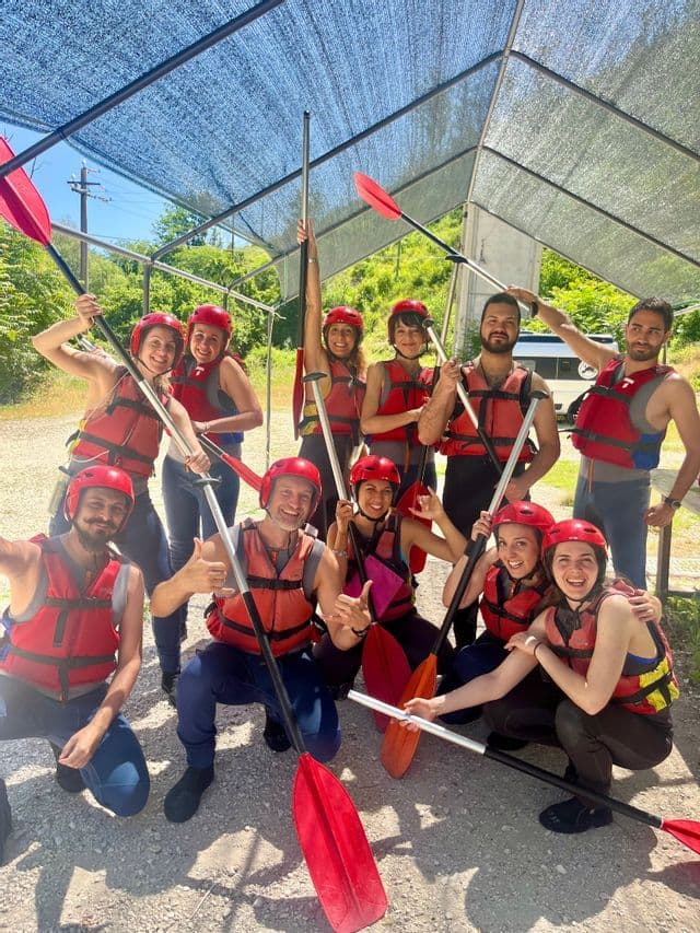Un gruppo WeRoad con caschi rossi e giubbotti di salvataggio sorride per una foto mentre tiene in alto le pagaie.