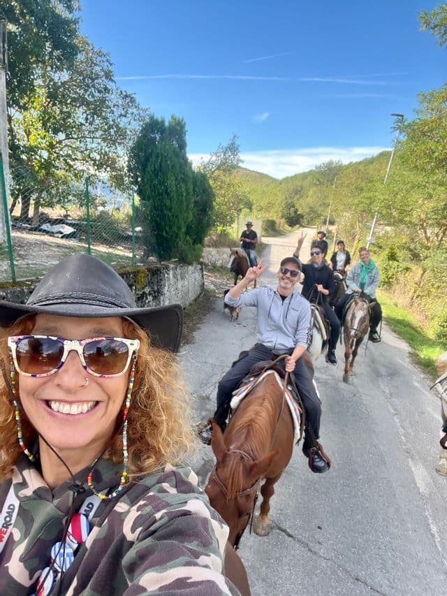 Una donna si scatta un selfie del suo viaggio di gruppo WeRoad a cavallo su una strada di campagna sotto un cielo blu.
