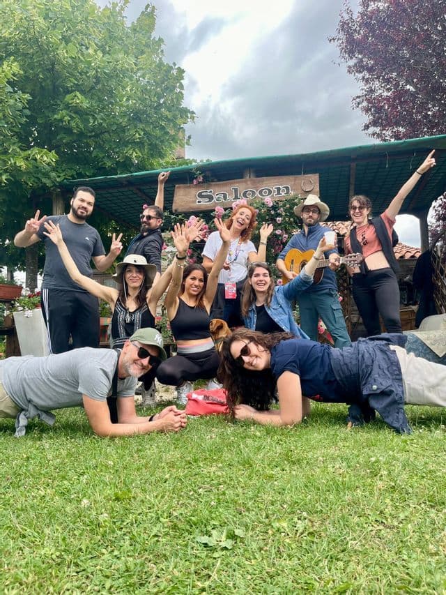 Un gruppo WeRoad in posa su un prato verde davanti a una struttura in legno con un'insegna 'Saloon'.