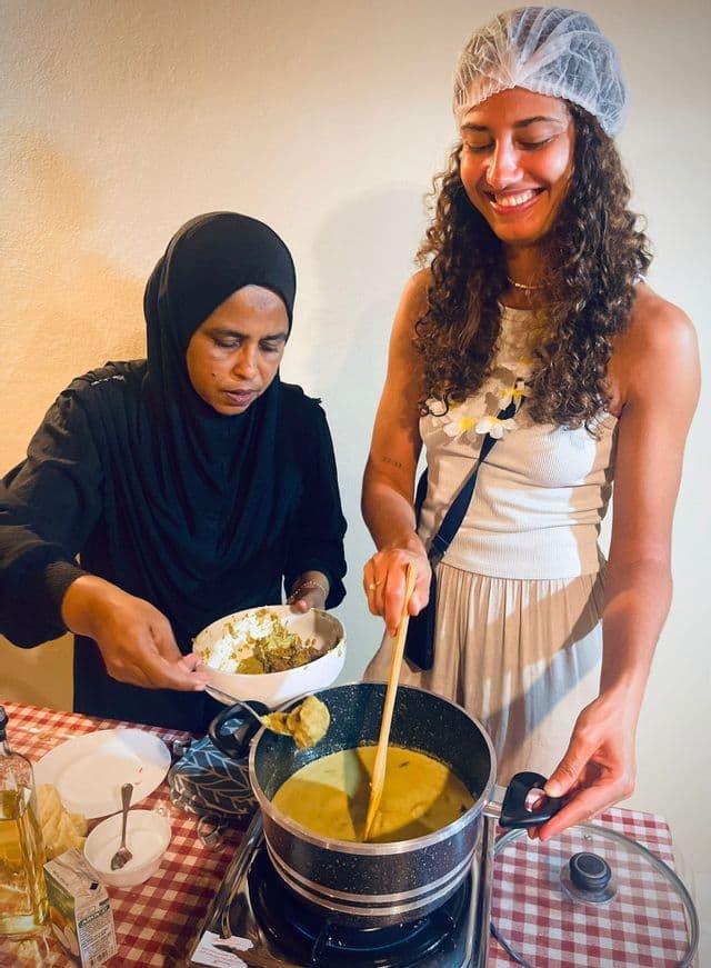 Deux femmes participant à un voyage de groupe WeRoad prennent part à un cours de cuisine, l'une remuant une casserole pendant que l'autre ajoute des ingrédients.
