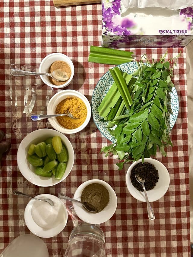 Un assortiment d'épices comme le curcuma et les grains de poivre, des herbes fraîches et des légumes dans des bols sur une nappe à carreaux.