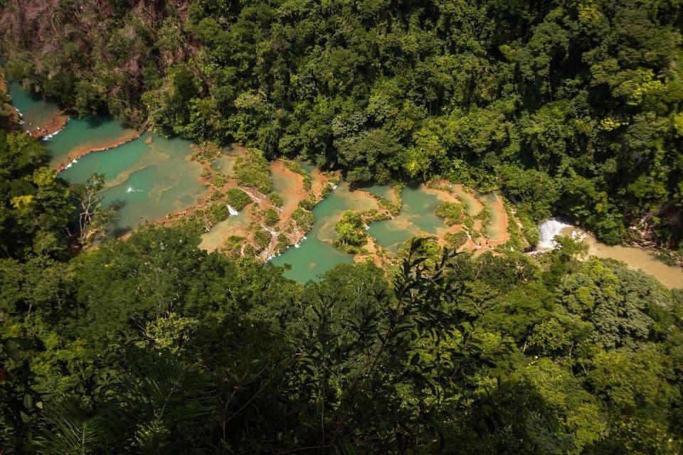 Una vista aérea de un viaje en grupo de WeRoad en piscinas escalonadas de agua turquesa en un río rodeado de una exuberante jungla verde.