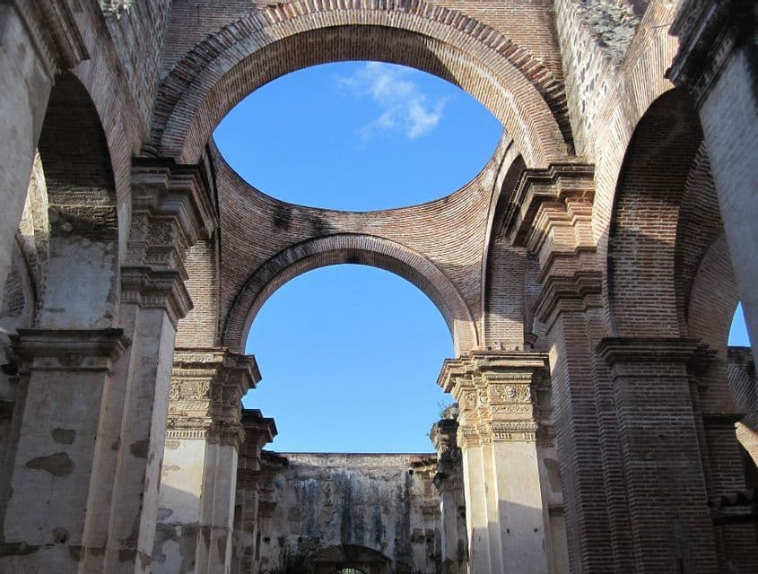 El interior de un edificio de ladrillo en ruinas y sin techo, con grandes arcos y columnas enmarcando un cielo azul claro.