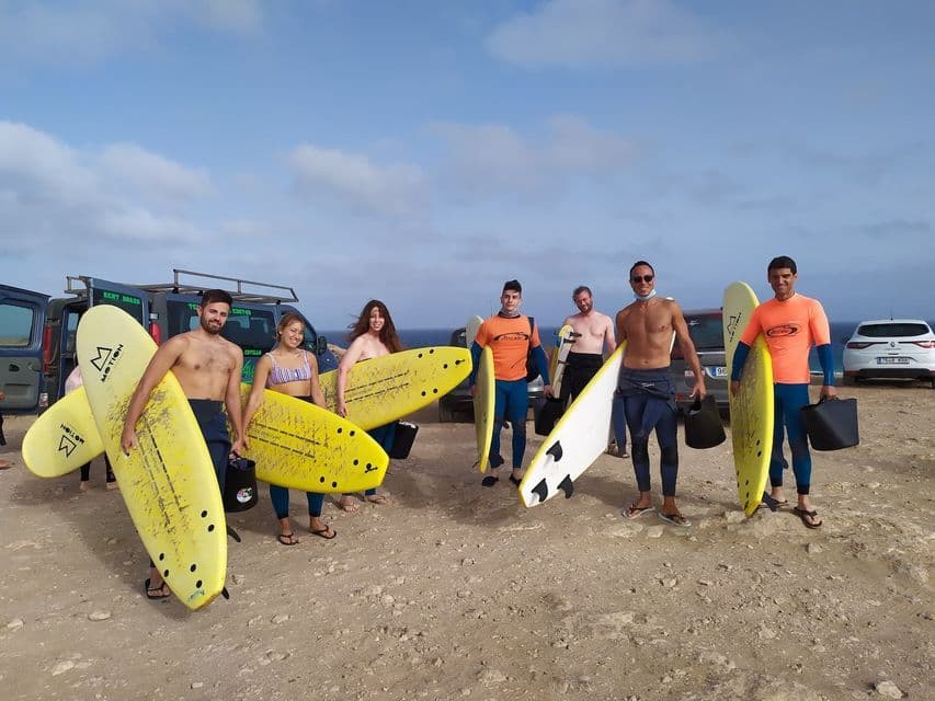 Un grupo WeRoad de siete personas posando con sus tablas de surf en un acantilado junto al mar.