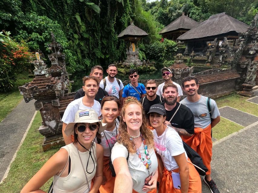A WeRoad group trip takes a selfie in front of an ornate stone temple surrounded by lush greenery.