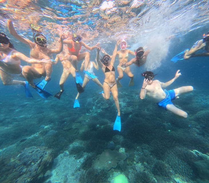 Eine WeRoad Gruppenreise mit Teilnehmern in Schnorchelausrüstung, die für ein Unterwasserfoto über einem Korallenriff posieren.