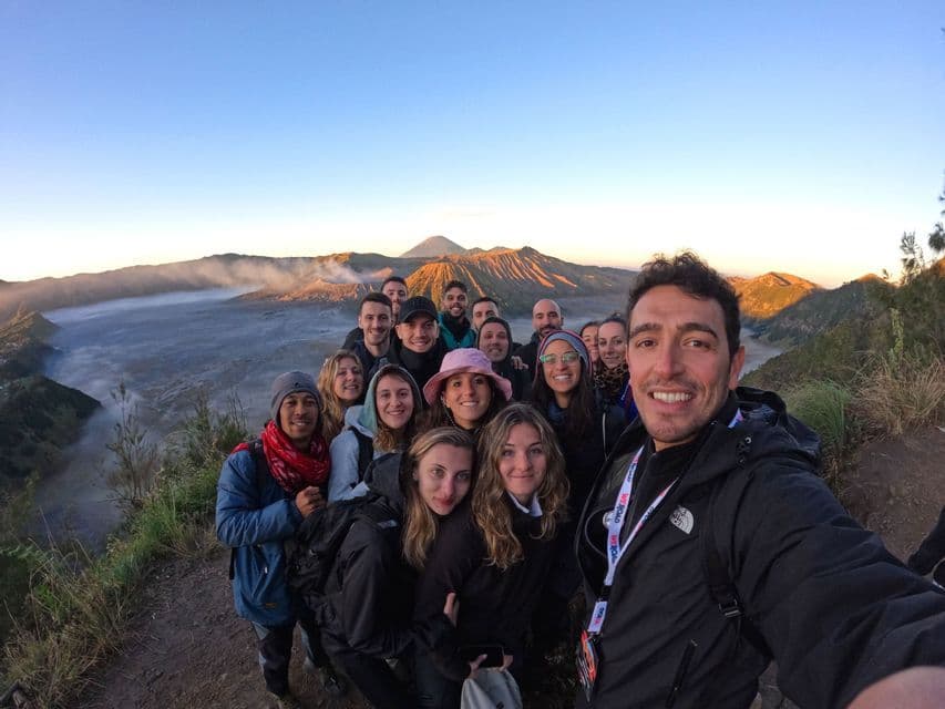 A WeRoad group trip takes a selfie on a viewpoint, with a volcanic caldera landscape in the background at sunrise.