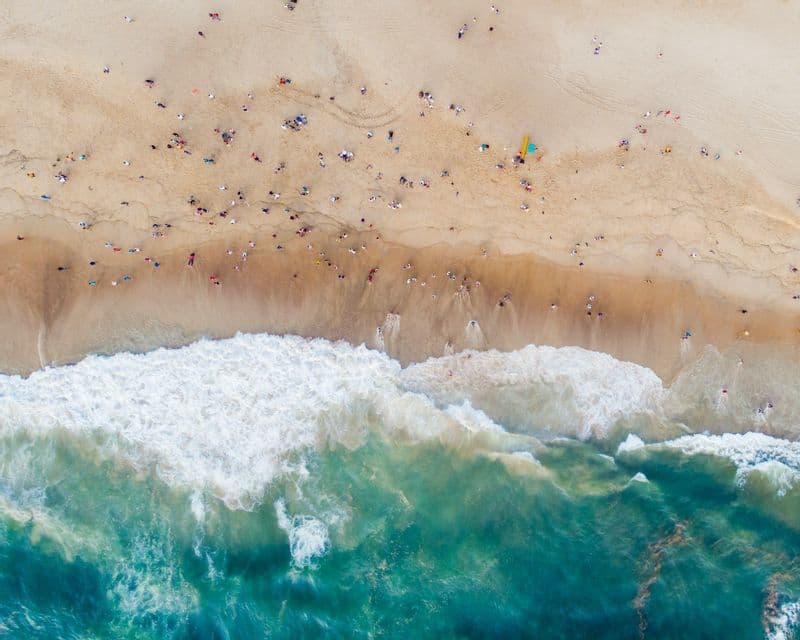 Una vista aerea dall'alto di molte persone su una spiaggia sabbiosa mentre onde bianche da un oceano turchese si infrangono a riva.