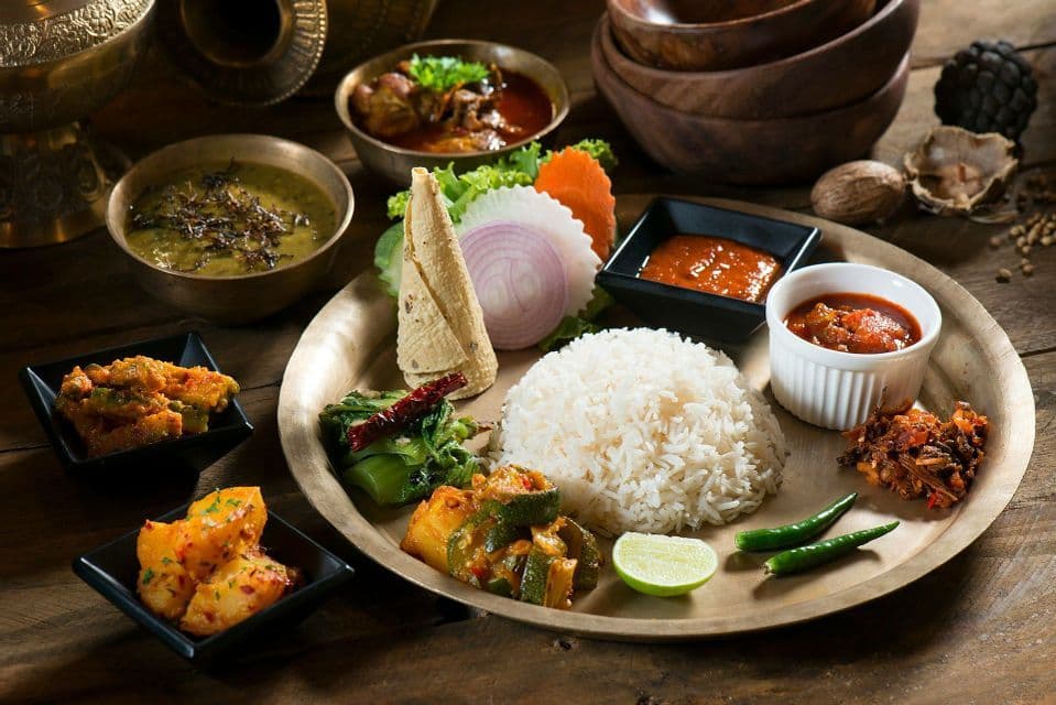 Un pasto thali tradizionale con riso, vari curry, dal e salse, servito su un grande piatto di ottone su un tavolo di legno.