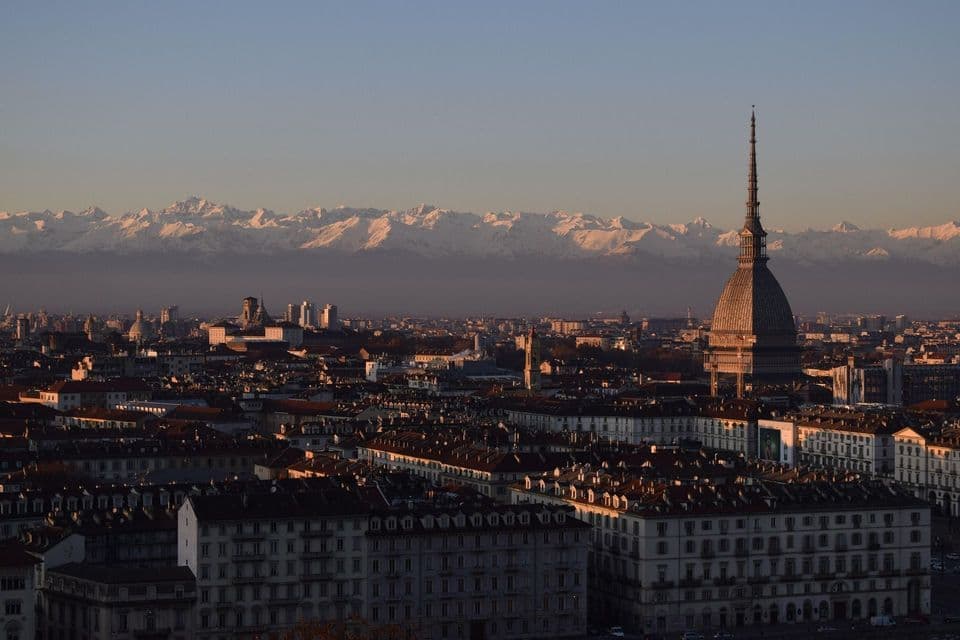 Un horizonte urbano con una distintiva cúpula, con el telón de fondo de una cordillera de montañas nevadas al atardecer.