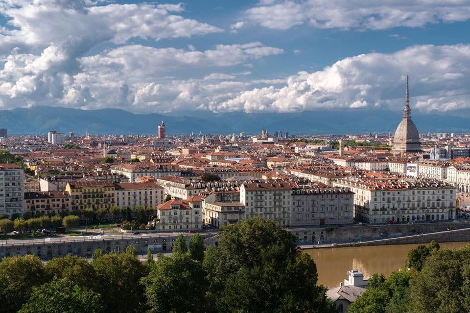 Vista aérea de un paisaje urbano con un río, un chapitel prominente y montañas distantes bajo un cielo azul nublado.