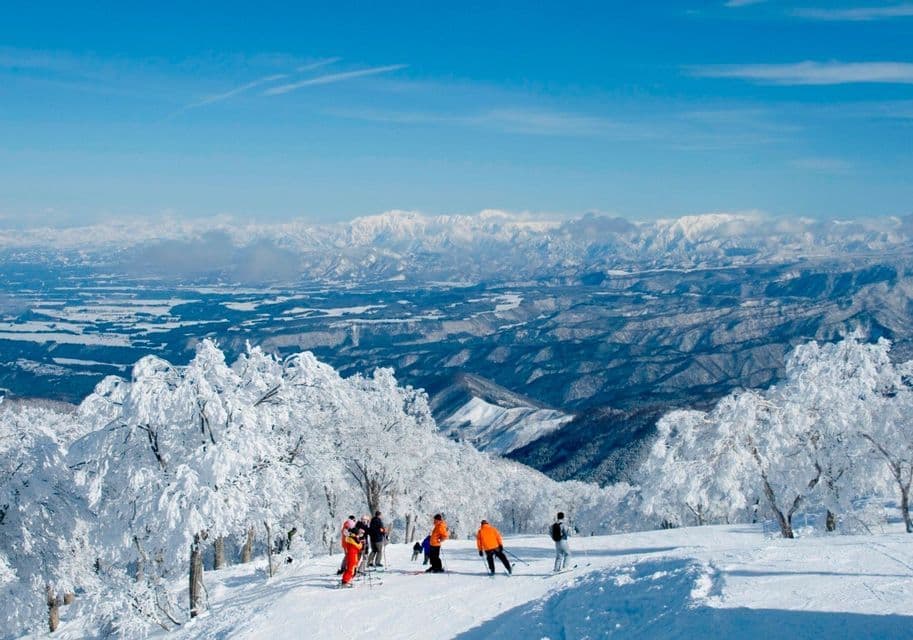Eine WeRoad-Gruppe von Skifahrern steht auf einem verschneiten Hang mit Blick auf ein weites, schneebedecktes Gebirgstal unter blauem Himmel.