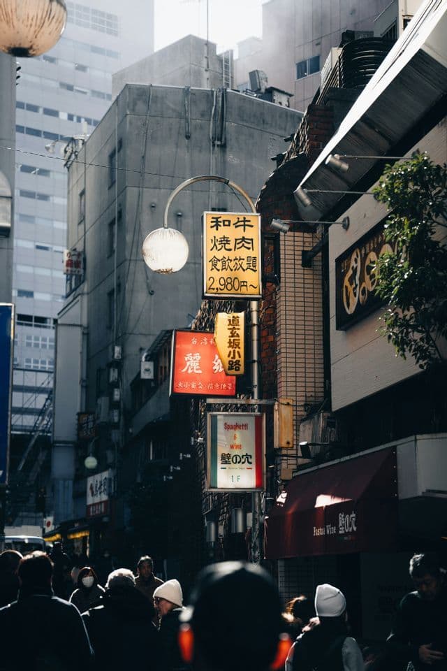 A crowded street in a Japanese city with many vertical signs and lanterns hanging overhead.