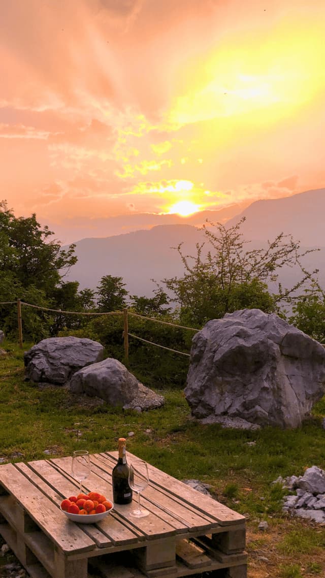 Una bottiglia di spumante e una ciotola di fragole su un tavolo di pallet di legno durante un tramonto in montagna.