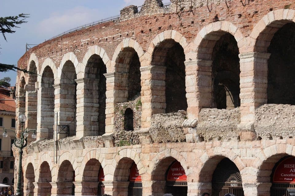 El exterior de un gran anfiteatro romano con arcos escalonados de piedra y ladrillo bajo un cielo despejado.