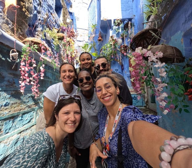 Un voyage de groupe WeRoad de six personnes souriantes prenant un selfie dans une ruelle étroite avec des murs bleu vif et des fleurs suspendues.