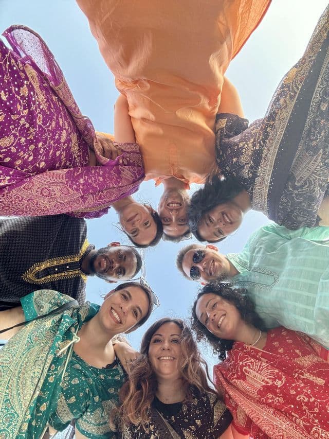 Un grupo de WeRoad con ropa tradicional colorida se agrupa en círculo, sonriendo a la cámara bajo un cielo despejado.