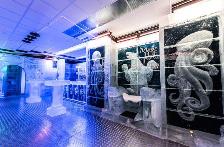 The interior of an ice bar with tables, a counter, and wall sculptures carved from ice, including octopuses and a polar bear.
