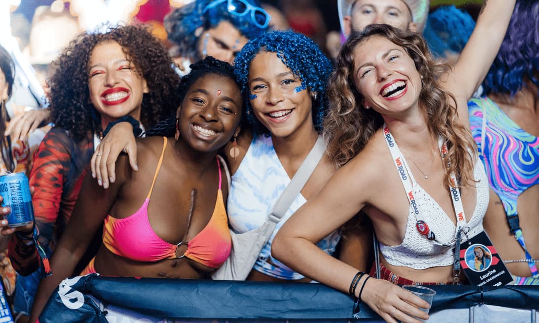 Un viaggio di gruppo WeRoad di quattro donne che sorridono e ridono insieme tra la folla a un festival all'aperto.