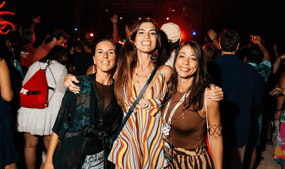 Tre donne di un viaggio di gruppo WeRoad sorridono e posano insieme a una festa notturna con una folla sullo sfondo.