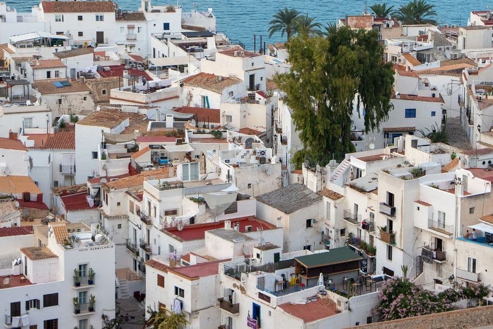 Una vista aérea de un pueblo costero con edificios encalados densamente agrupados y tejados de terracota junto al mar azul
