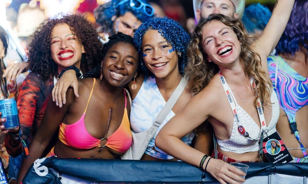 Quattro donne in viaggio di gruppo WeRoad sorridono e ridono insieme a un affollato festival musicale.