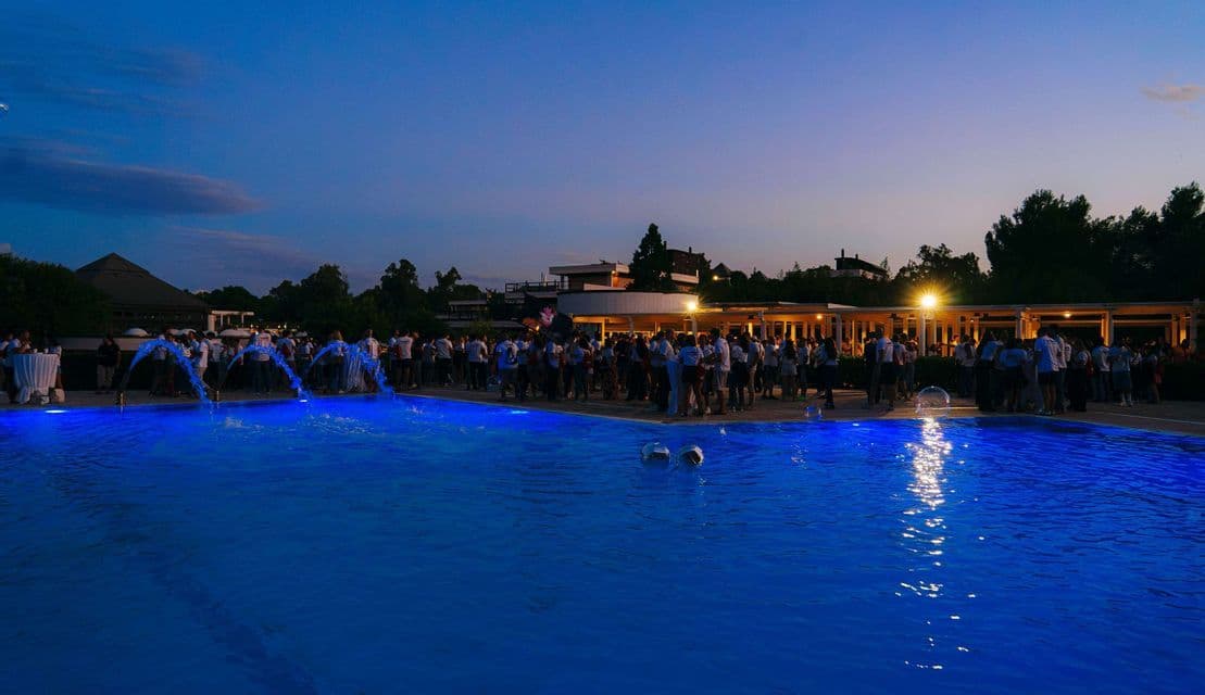 Un viaggio di gruppo WeRoad che si riunisce attorno a una piscina illuminata da luci blu e fontane al tramonto.
