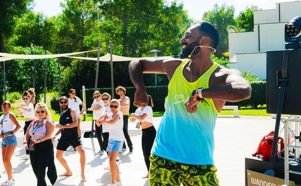 Un istruttore uomo con auricolare guida un viaggio di gruppo WeRoad a una lezione di fitness danza all'aperto.