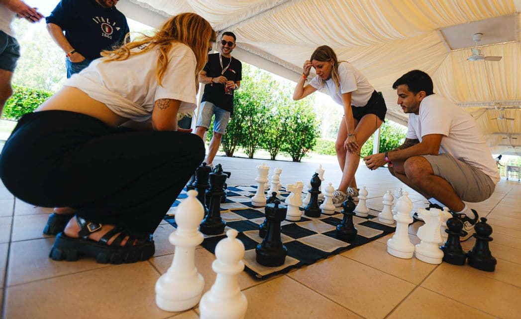 Un viaggio di gruppo WeRoad si raduna attorno a una scacchiera gigante a terra, giocando una partita sotto una tettoia esterna.