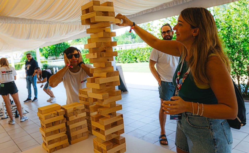 Una donna di un gruppo WeRoad sfila un pezzo da un'alta torre di legno mentre un uomo osserva con ansia.