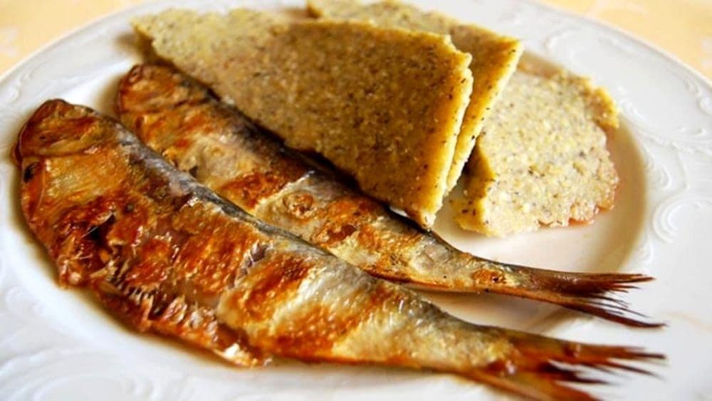 Un primo piano di due pesci interi alla griglia e fette di polenta disposti su un piatto bianco.