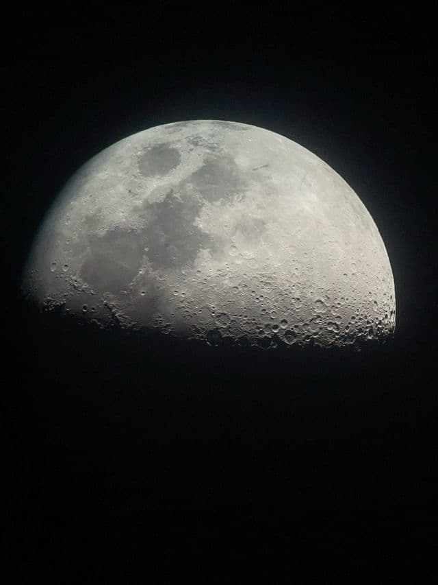 Un primo piano dettagliato della luna gibbosa, che rivela numerosi crateri sulla sua superficie illuminata contro un cielo nero.