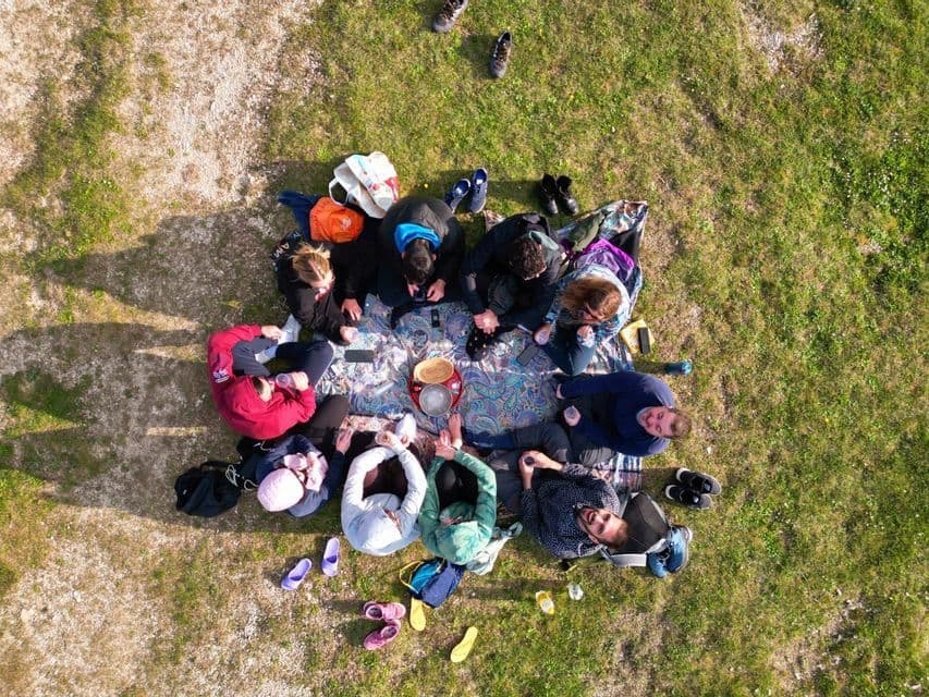 Un gruppo WeRoad seduto in cerchio su una coperta da picnic in un prato, visto dall'alto.