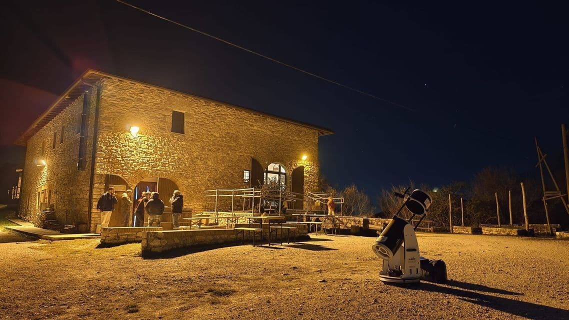 Un viaggio di gruppo WeRoad si riunisce fuori da un edificio in pietra illuminato di notte, con un grande telescopio installato per l'osservazione delle stelle.