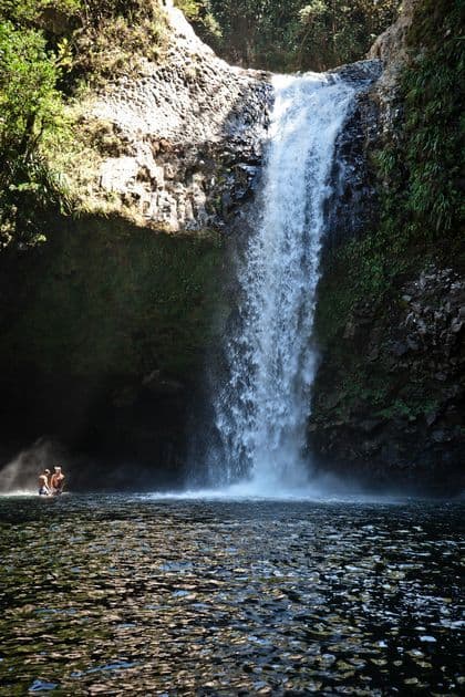 Un voyage de groupe WeRoad se baignant dans l'eau au pied d'une grande cascade entourée de falaises rocheuses.