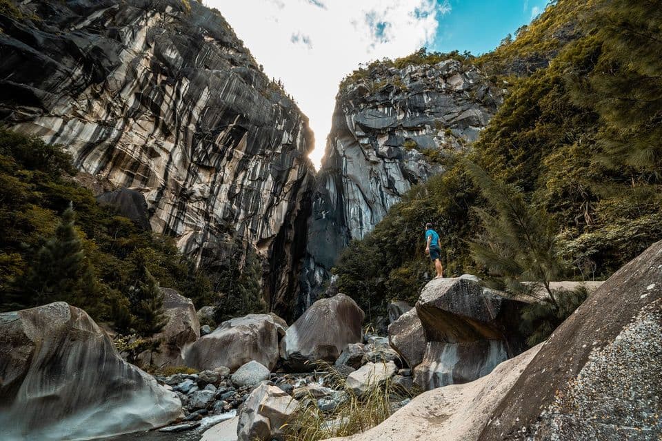 Une personne se tient sur un grand rocher au fond d'un canyon spectaculaire avec de hautes parois rocheuses rayées.