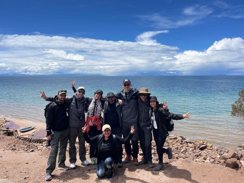 Un gruppo WeRoad in viaggio posa per una foto su una costa rocciosa, con un grande specchio d'acqua e un cielo parzialmente nuvoloso alle spalle.