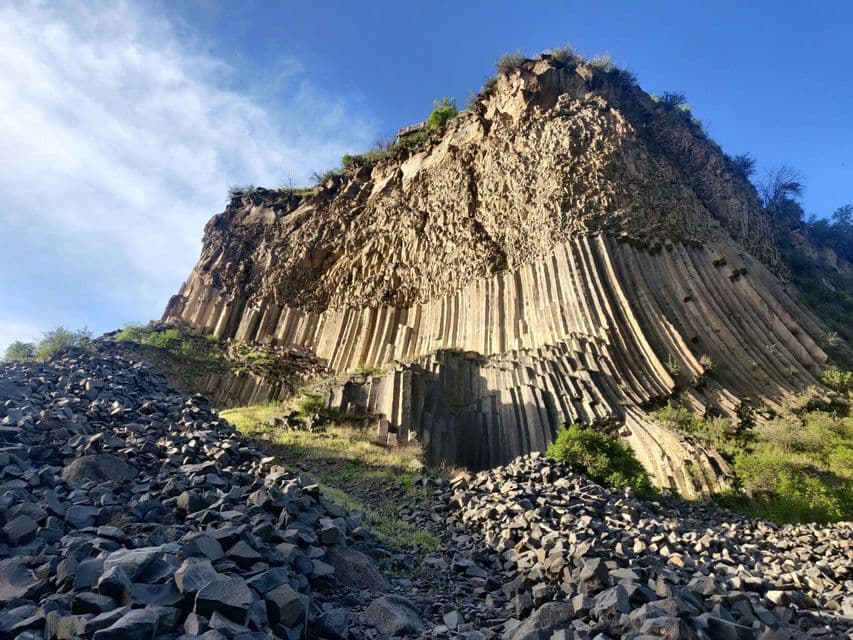 Un'imponente scogliera di formazioni di basalto colonnare si erge sotto un cielo azzurro, con rocce spezzate che ricoprono il terreno sottostante.