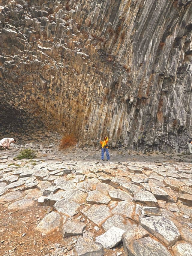 Una donna in un viaggio di gruppo WeRoad si trova su colonne esagonali di basalto all'interno di una massiccia formazione rocciosa ricurva.
