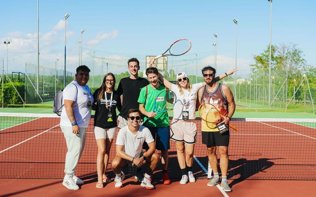 Un viaje en grupo de WeRoad con personas sonriendo y posando juntas con raquetas en una cancha de tenis al aire libre.