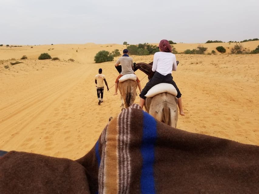 Un voyage de groupe WeRoad à dos de chameau en file indienne à travers un désert de sable, mené par un guide.