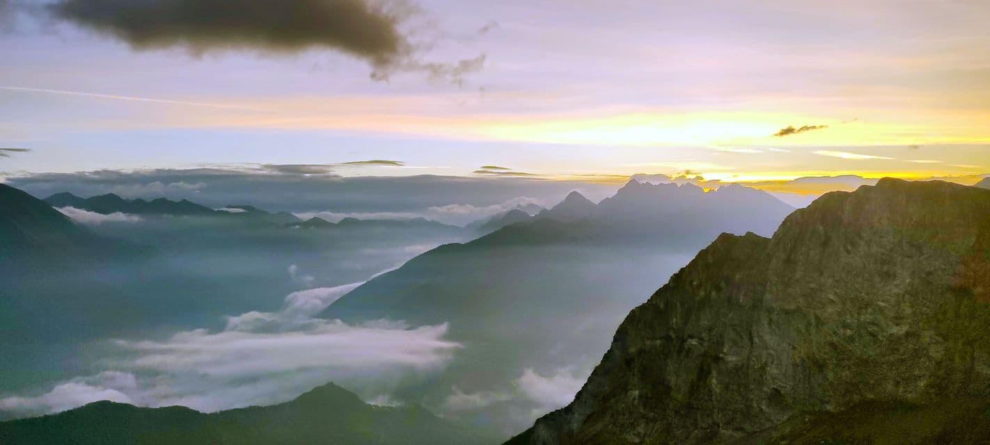 Una vasta catena montuosa con nuvole basse che riempiono le valli, vista all'alba con una luce dorata all'orizzonte.